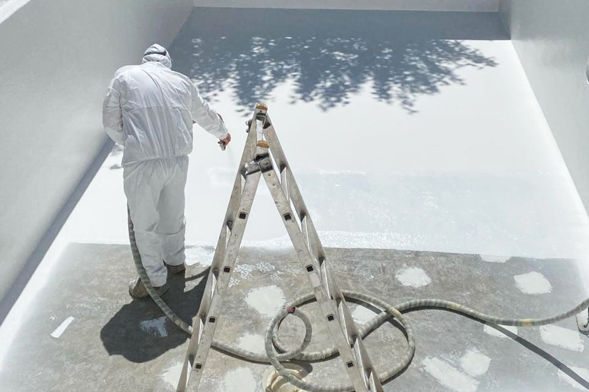 Ein Mann in weißer Schutzkleidung besprüht einen leeren Pool mit weißer Farbe
