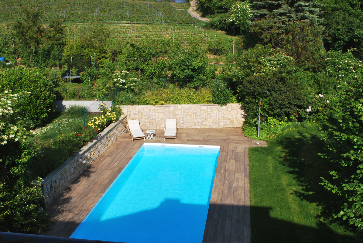 Aufnahme eines gepflegten Gartens mit eingebautem Pool im Sommer. Hinter dem Pool stehen moderne Liegen.