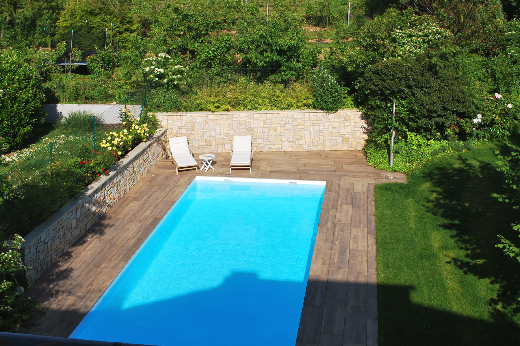 Aufnahme eines gepflegten Gartens mit eingebautem Pool im Sommer. Hinter dem Pool stehen moderne Liegen.